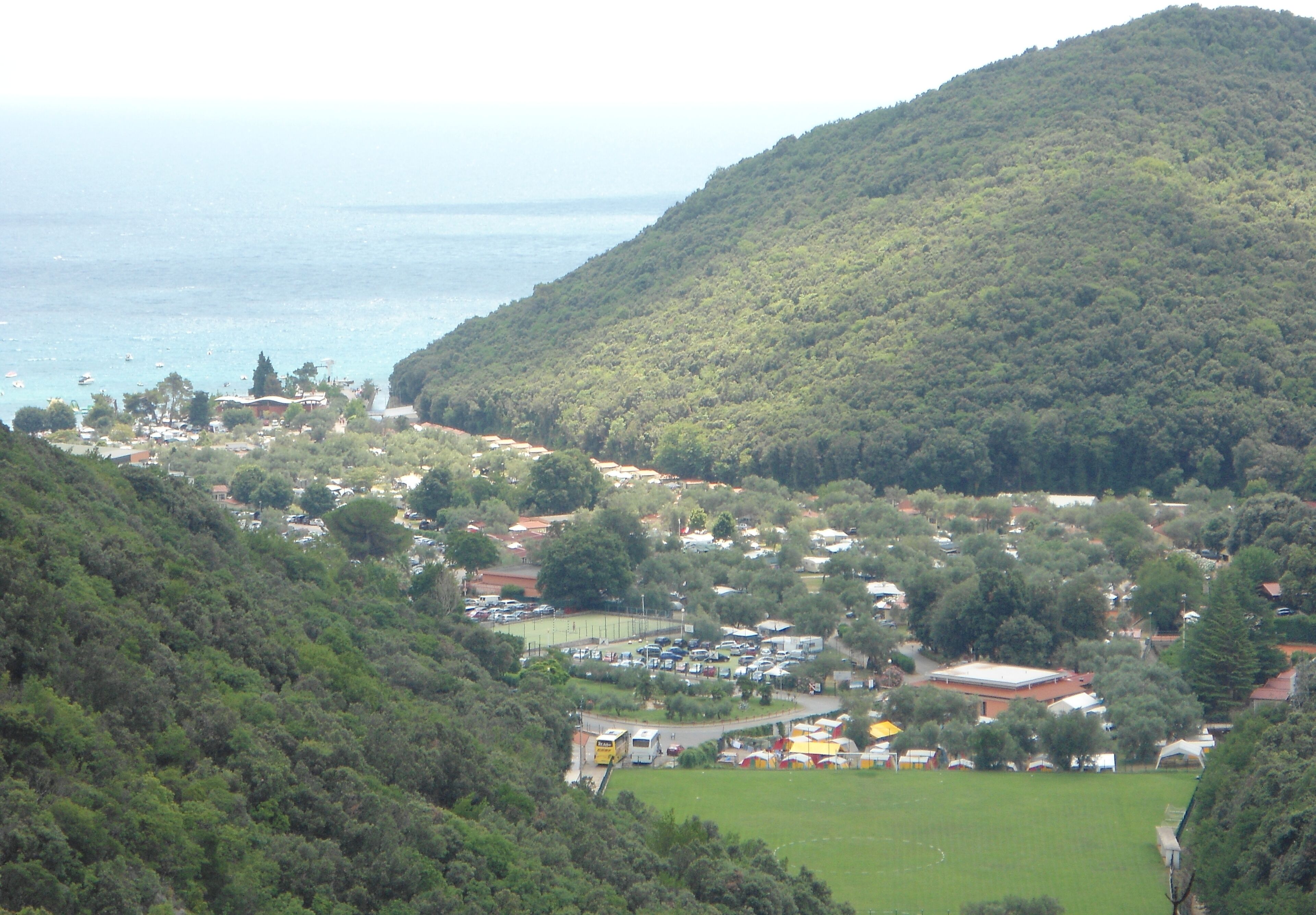 A coastal town with a hill, a marina, and a green field.