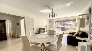 Ein modernes Wohnzimmer mit einem runden Marmortisch, weißen Stühlen, einem braunen Sofa und einem großen Fenster mit Stadtblick.
