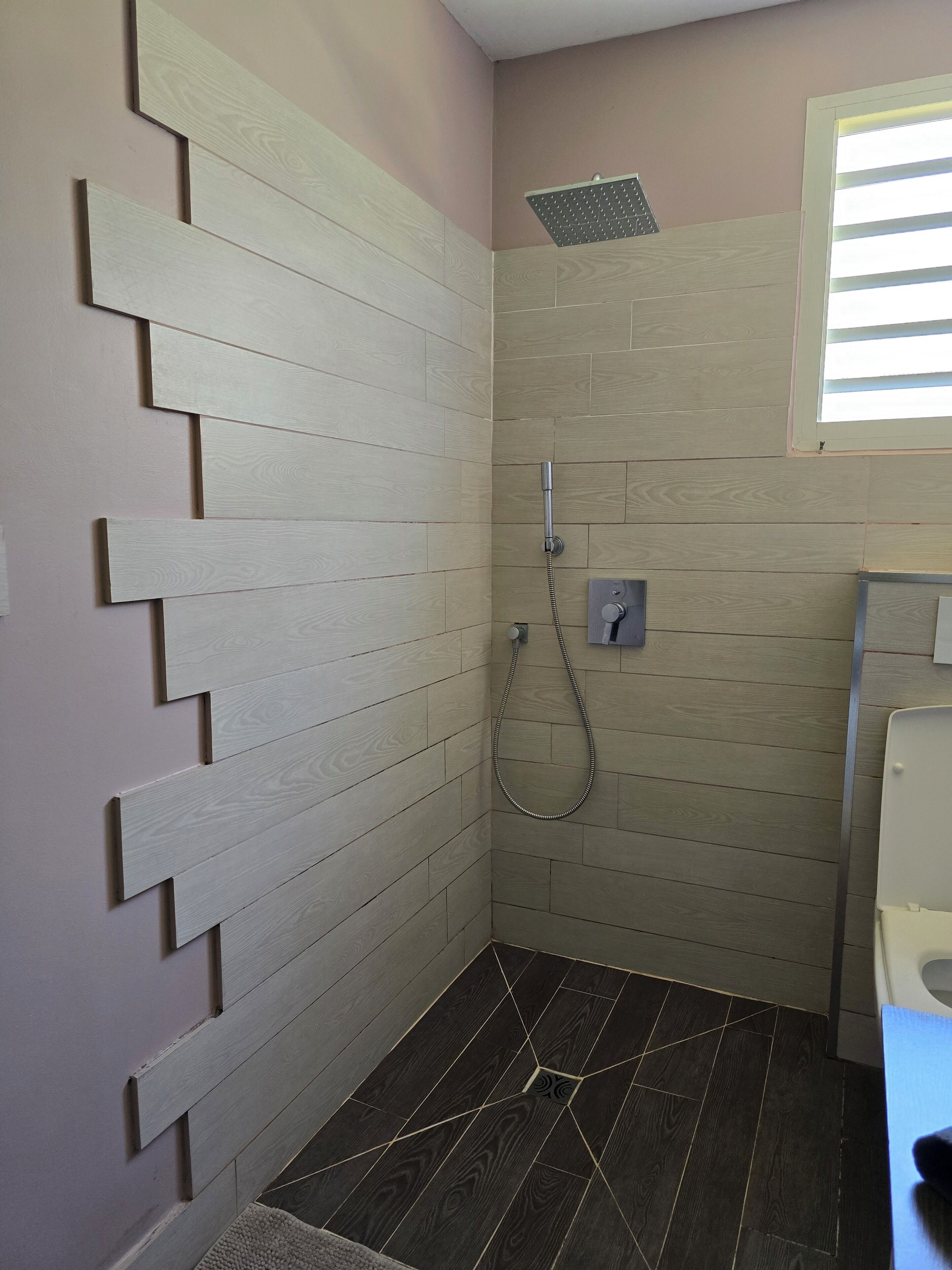 A bathroom with a shower, tiled walls, and a dark wood floor.