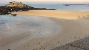 A beach with a castle-like structure on a rocky outcrop, a sandy beach, and a calm sea. - Gite Breton house close to the Rance and the sea Saint-Malo Dinard Cancale (Pleudihen-Sur-Rance)