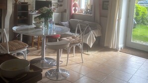 A dining area with a round table, chairs, and a window with curtains. - Gite Breton house close to the Rance and the sea Saint-Malo Dinard Cancale (Pleudihen-Sur-Rance)