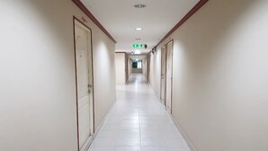 A long, narrow hallway with white tiled floors and cream-colored walls, leading to a door at the end.