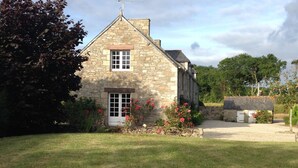 Une maison en pierre avec un petit jardin et un grand rocher au premier plan.