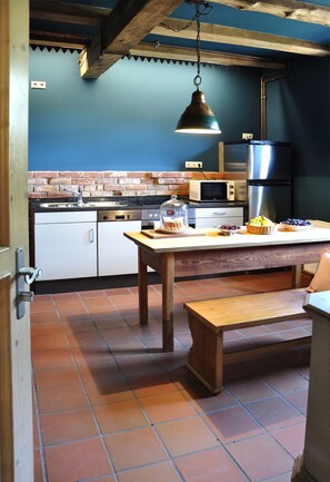 Compact kitchen with a rustic table, pendant light, and brick wall, featuring a microwave, refrigerator, sink, and dishwasher.
