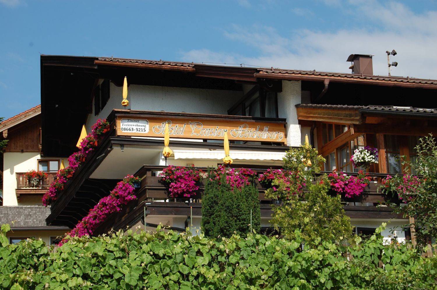 Ein Hotel mit Balkon, der mit Blumen geschmückt ist, einem Schild mit Kontaktinformationen und traditioneller Architektur.