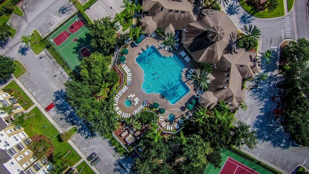 An aerial view of a resort with a central swimming pool, tennis courts, and a landscaped area with palm trees. - GREAT PRICE! TOP RESORT! On Disney's Doorstep! (Kissimmee)