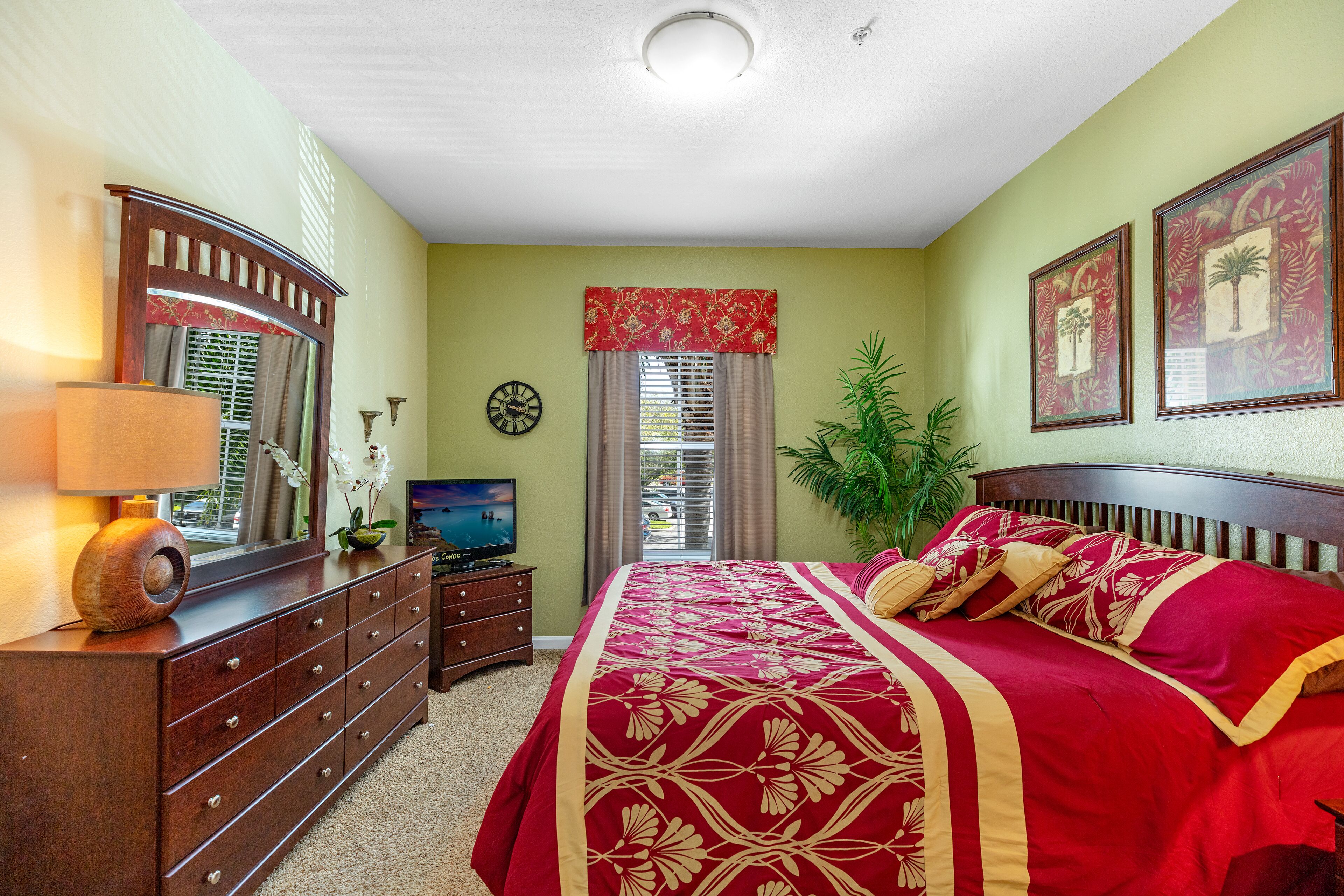 A bedroom with a large bed, a dresser, a television, and a window with curtains.