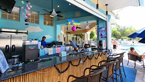A bar area with a counter, seating, and a pool in the background. - GREAT PRICE! TOP RESORT! On Disney's Doorstep! (Kissimmee)