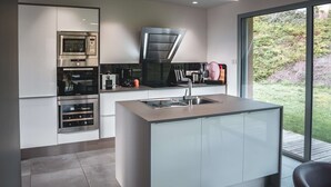 A modern kitchen with built-in appliances, a large island with a sink, and a view of the outdoors.