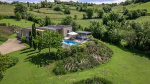 A modern house with a swimming pool, surrounded by lush greenery and hills.