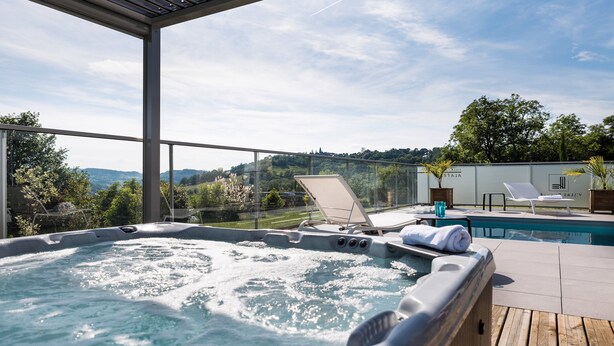A hot tub with a wooden deck, lounge chairs, and a poolside area with a view of the hills.