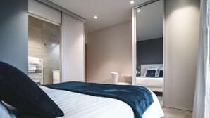 A modern hotel room with a large bed, a walk-in closet, a bathroom with a shower, and a view of the city.