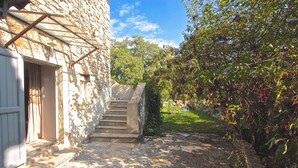 Un bâtiment en pierre avec un escalier menant à une porte, entouré de verdure et sous un ciel dégagé.
