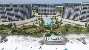 Un hotel de gran altura con piscina central rodeada de palmeras y una zona de playa con tumbonas.