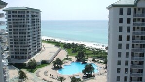 Un resort con piscina central rodeada de zonas de descanso y palmeras, con vistas a una playa.