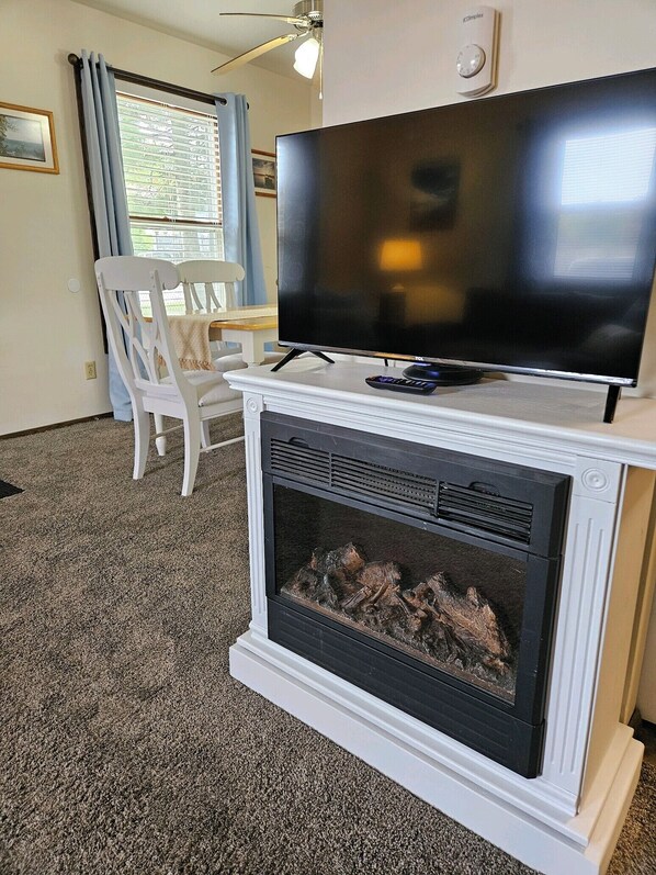 A living room with a fireplace, a television on a stand, a white chair, and a dining table.