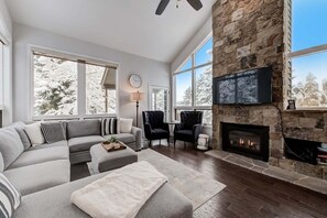 Cozy living room with a fireplace, large TV, and comfortable seating area offering a view of snow-covered trees.