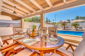 An outdoor dining area with a pool, wooden furniture, and a view of the ocean.