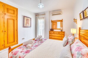 A hotel room with a bed, a dresser, a mirror, a window with curtains, and an air conditioning unit.