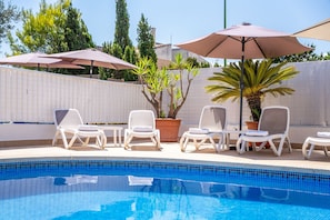 A poolside area with lounge chairs and umbrellas, a tiled pool, and potted plants.
