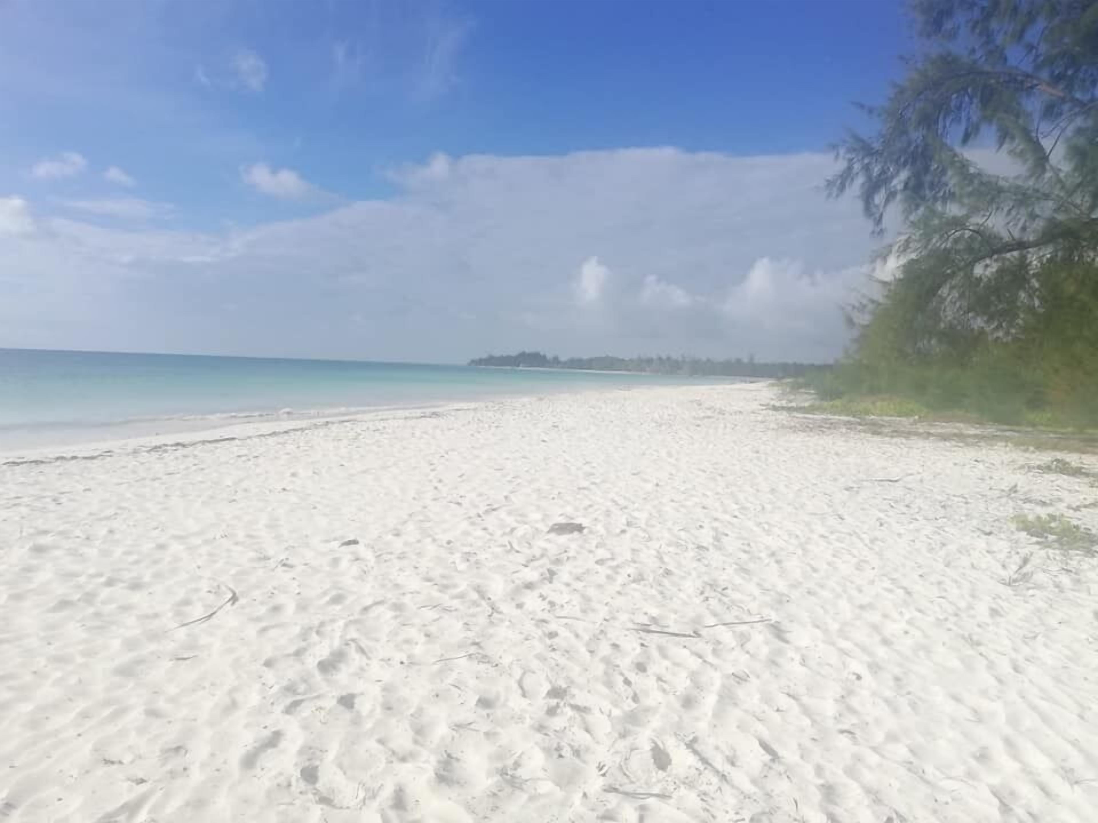 A wide, white sandy beach with clear blue water and a distant island.