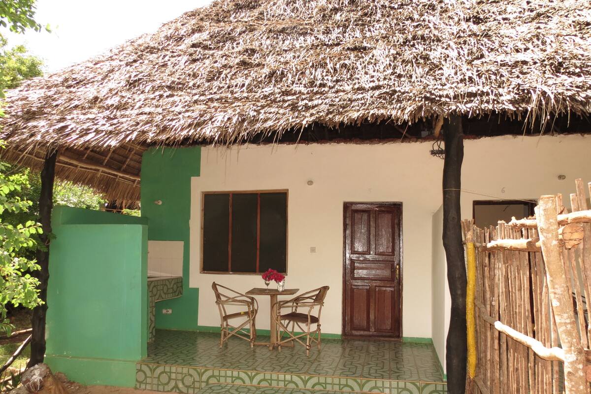 A house with a thatched roof, a green exterior wall, and a tiled porch.