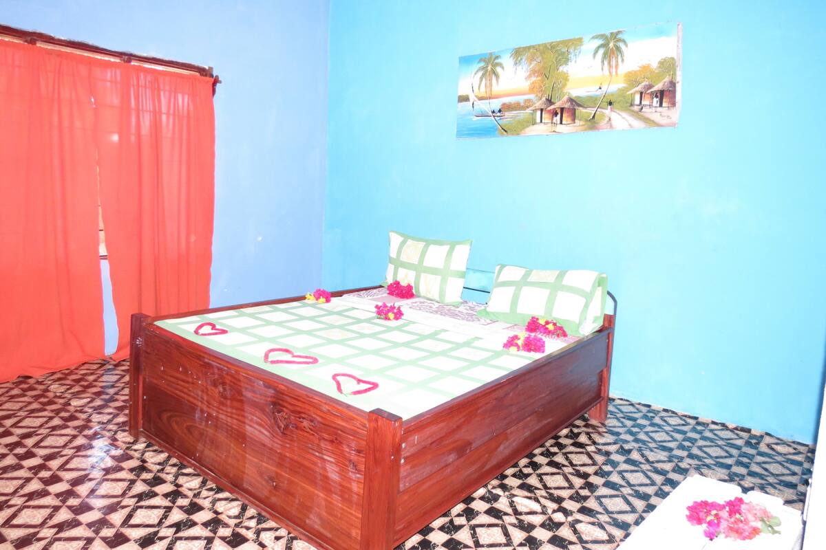 A bedroom with a bed, a picture on the wall, and a red curtain.