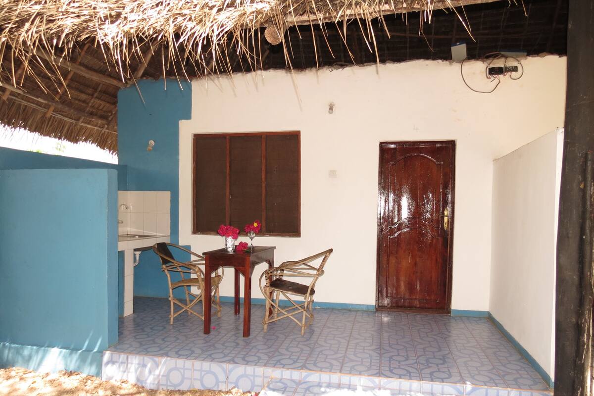 A room with a thatched roof, a window, a door, and a tiled floor.