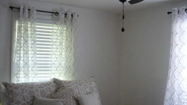 A bedroom with a bed, patterned pillows, a ceiling fan, and a window with blinds.