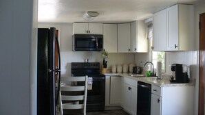 A compact kitchen with white cabinets, a black microwave, a stove, and a dishwasher.