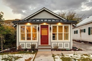 Una casa pequeña de un piso con puerta roja, detalles blancos y el número '1114' sobre la puerta.