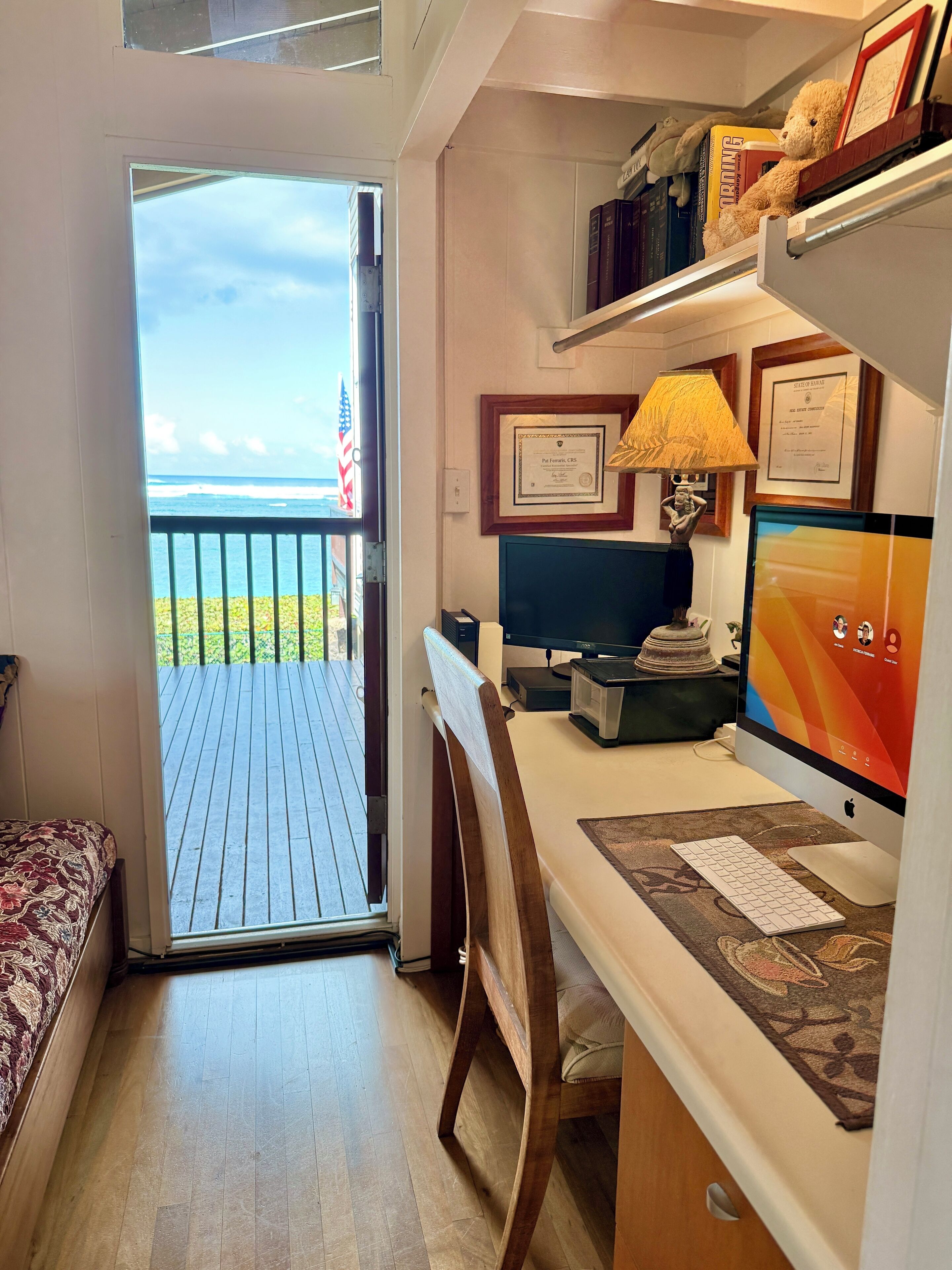 A room with a desk, computer, and a view of the ocean through a door.