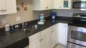 A kitchen with white cabinets, a double sink, a dishwasher, a stove, and a microwave. - Gulf Beach Apartment - with Pool & Beach Access  (Holmes Beach)