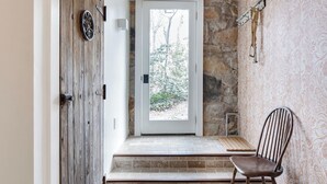 Una habitación con pared de piedra, puerta de madera, un banco y una silla.