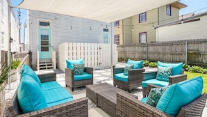 Un patio con mobiliario de mimbre y cojines color turquesa, una valla blanca y un edificio al fondo.