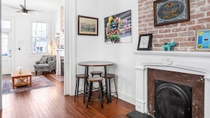 Una habitación con chimenea, una mesa de comedor con taburetes y una pared de ladrillo decorada con cuadros.