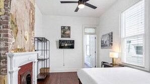 Un dormitorio con cama, chimenea, ventilador de techo, televisor y ventana con persianas.