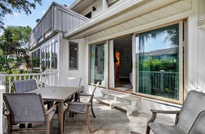 A wooden deck with a table and chairs, a bench, and a sliding glass door leading to an interior space.