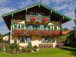 Um edifício de dois andares com varandas decoradas com flores, telhado verde e gramado bem cuidado.