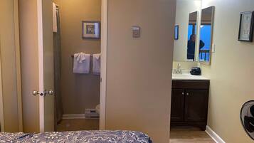 A hotel room with a bed, a bathroom with a shower, a sink, and a mirror.