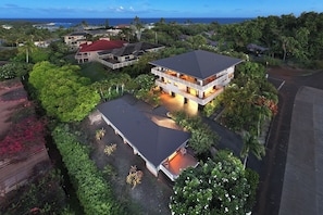 Une maison à deux étages dotée d’une grande terrasse et d’une piscine, entourée d’une végétation luxuriante et offrant une vue sur l’océan.