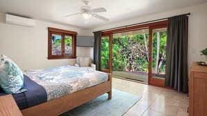 Een slaapkamer met een bed, een bureau, een stoel, een plafondventilator, een raam en een schuifdeur naar een tuin.