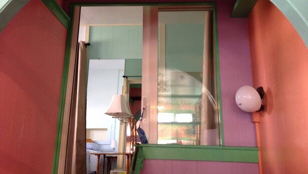 A room with a green-framed window, a lamp, and a view of the outside.