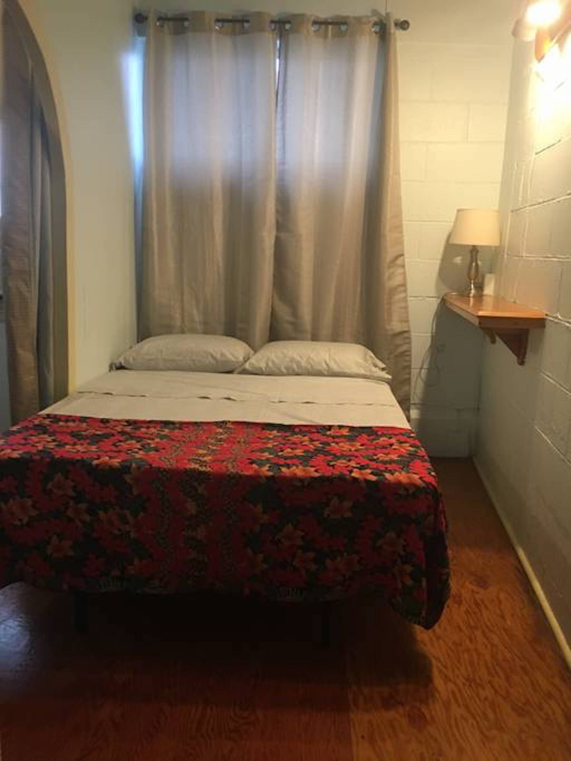 A small, narrow room with a bed, a nightstand, and a lamp.