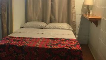 A small, narrow room with a bed, a nightstand, and a lamp.