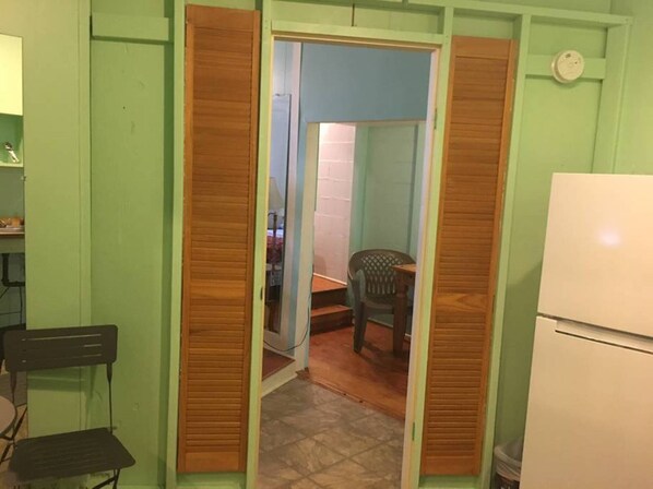 A compact kitchen with a refrigerator, a wooden door, and a chair.