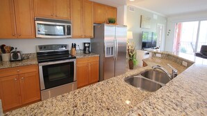 A modern kitchen with granite countertops, stainless steel appliances, wooden cabinets, and a built-in microwave. - Spacious Poolside End Unit! (Bonita Springs)