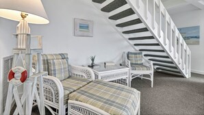 Een kamer met een witte wicker loungeset, een klein tafeltje, een lamp en een trap met een gestructureerde muur.