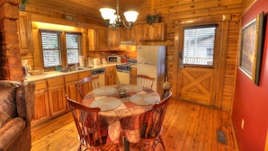 A wooden cabin interior with a dining table, chairs, kitchen area, and wooden walls.