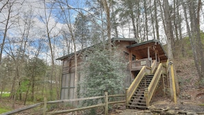 A cabin with a wooden exterior, a balcony, and a staircase leading to the upper level.